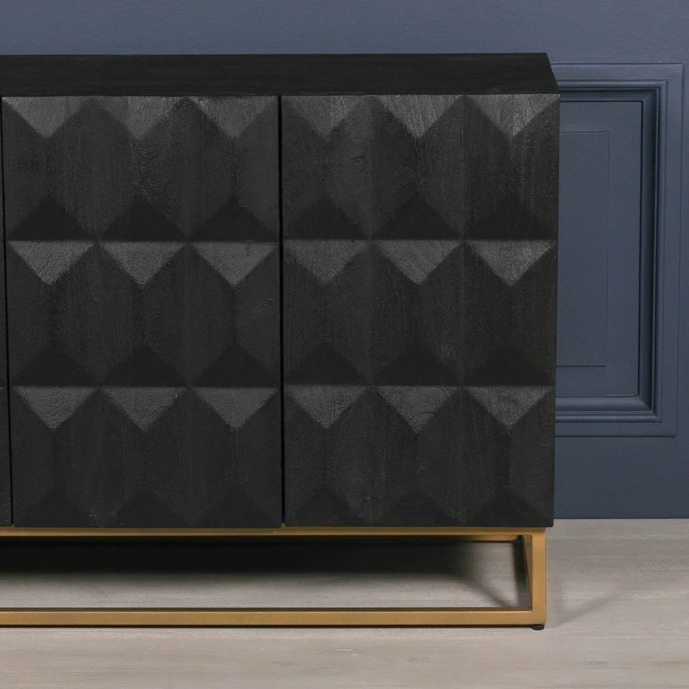 Black sideboard with geometric textured doors and gold metal base against blue wall