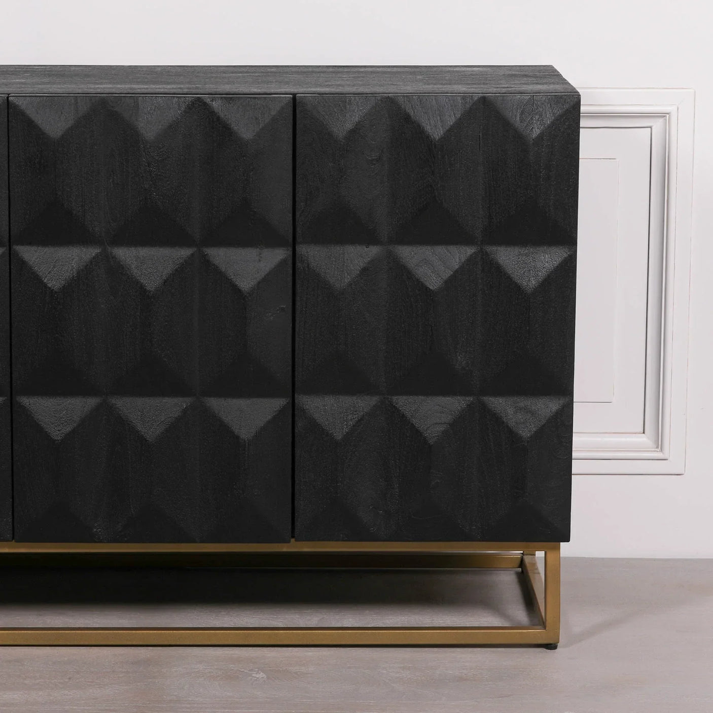 Black sideboard with geometric textured doors and gold metal base against white wall