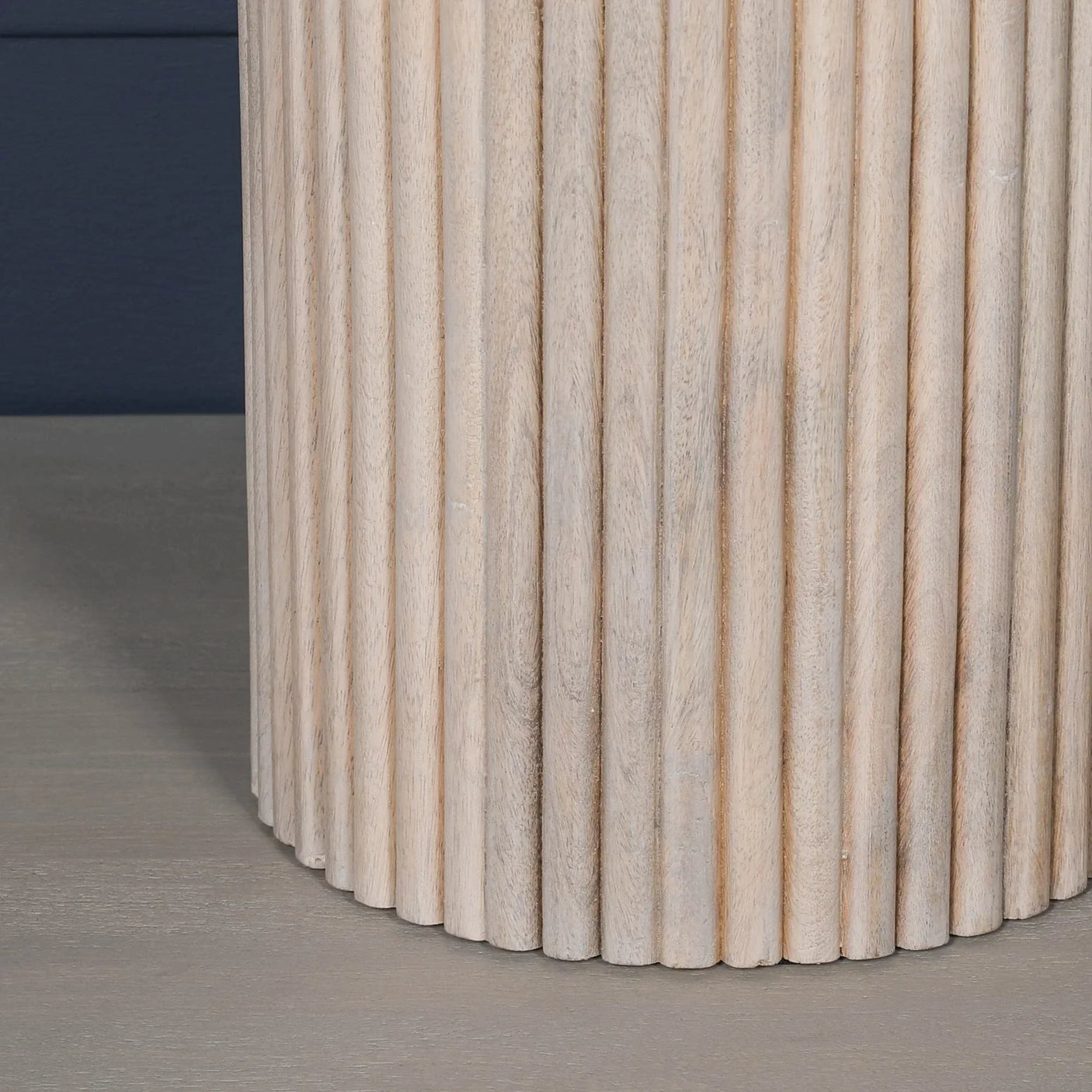 close-up of ribbed wooden table base with light natural finish on grey floor