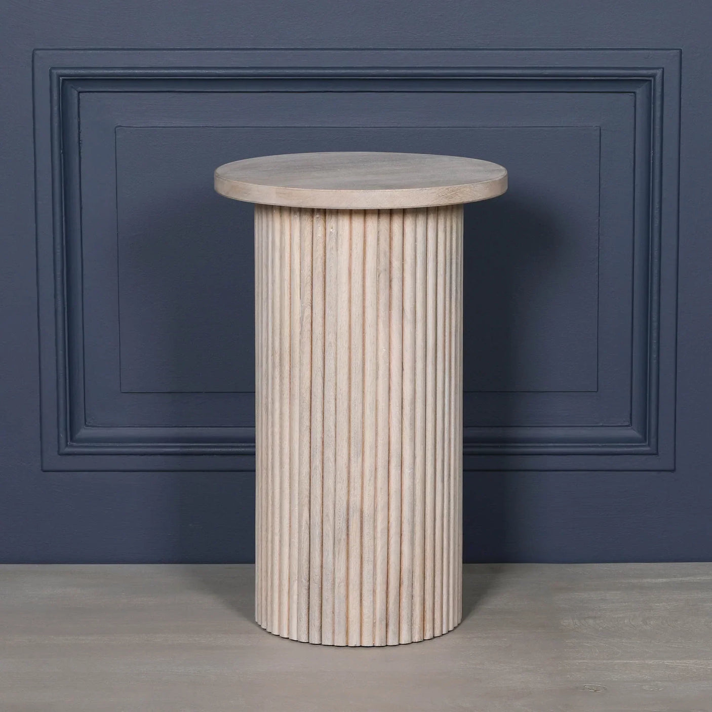 Round fluted wooden side table with light finish against dark blue wall