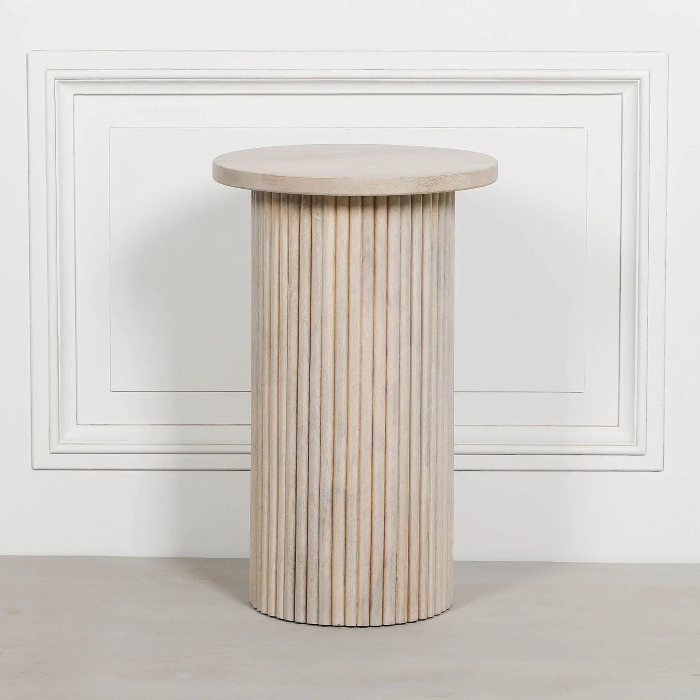 Light oak fluted side table with round top placed against white panel wall