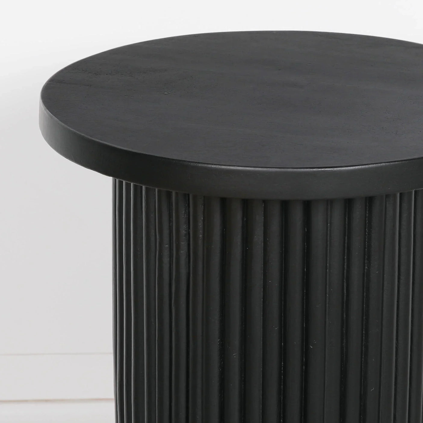 Black round side table with fluted base and smooth top against white background