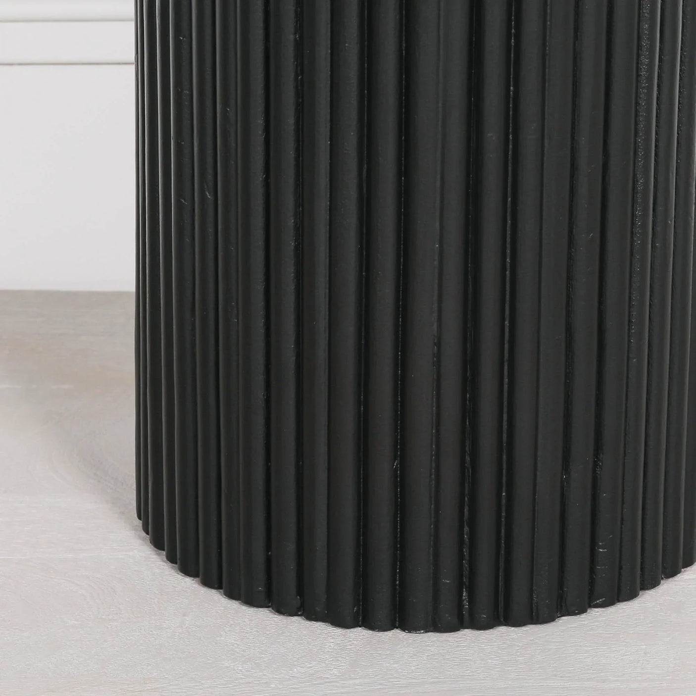 Black ribbed cylindrical table base on light wood floor