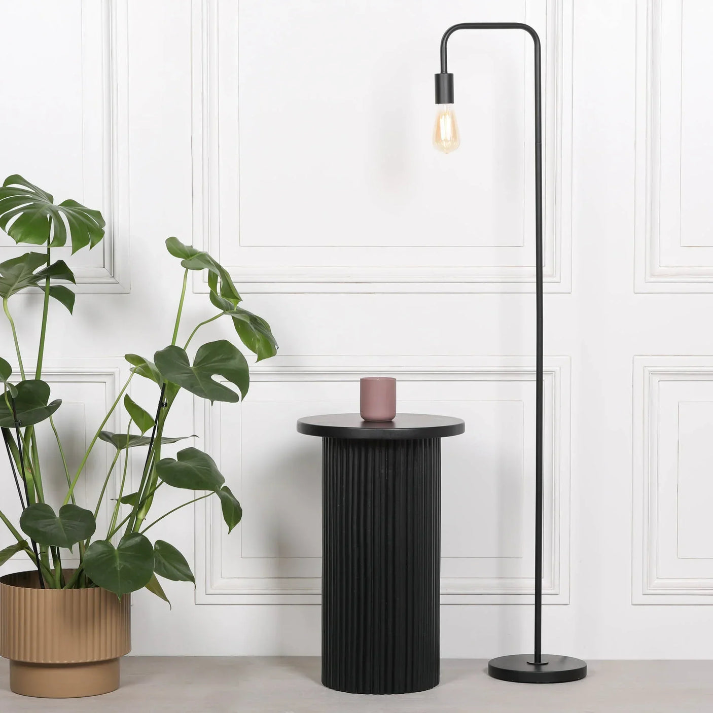 Black round side table with grooved base beside floor lamp and potted plant in modern room