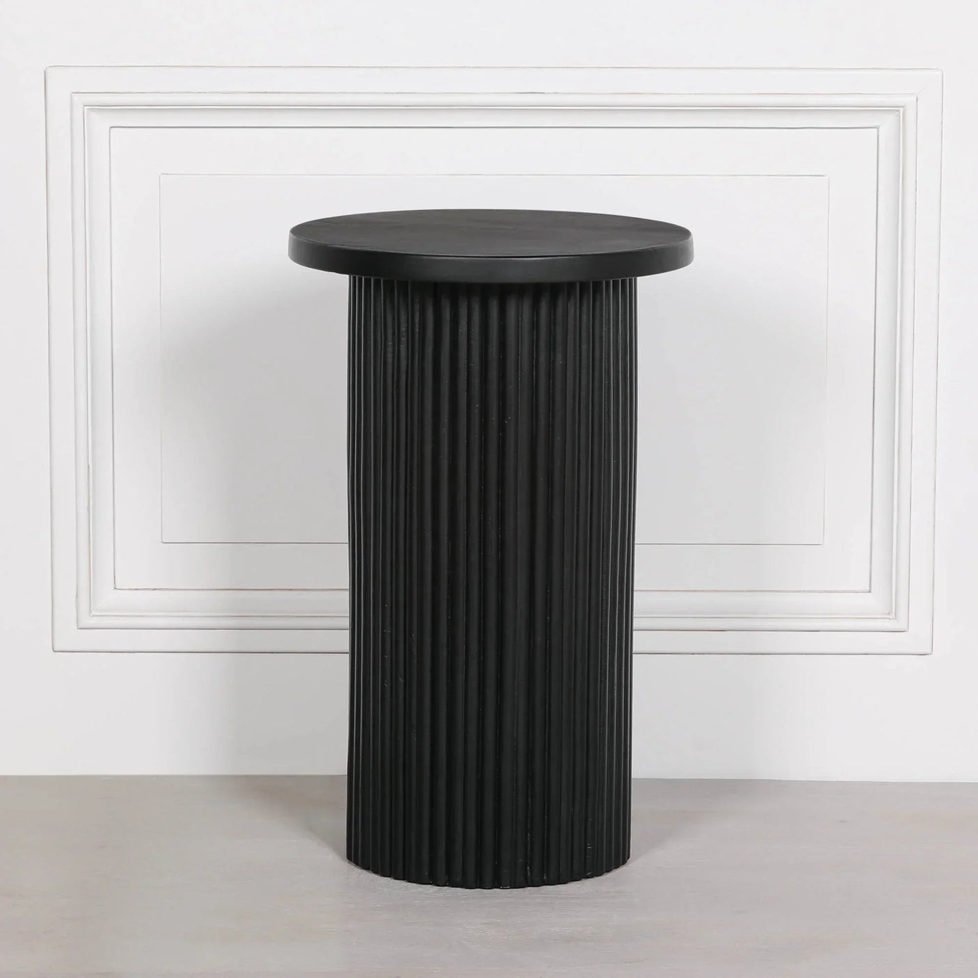 Black ribbed side table with round top against white paneled wall