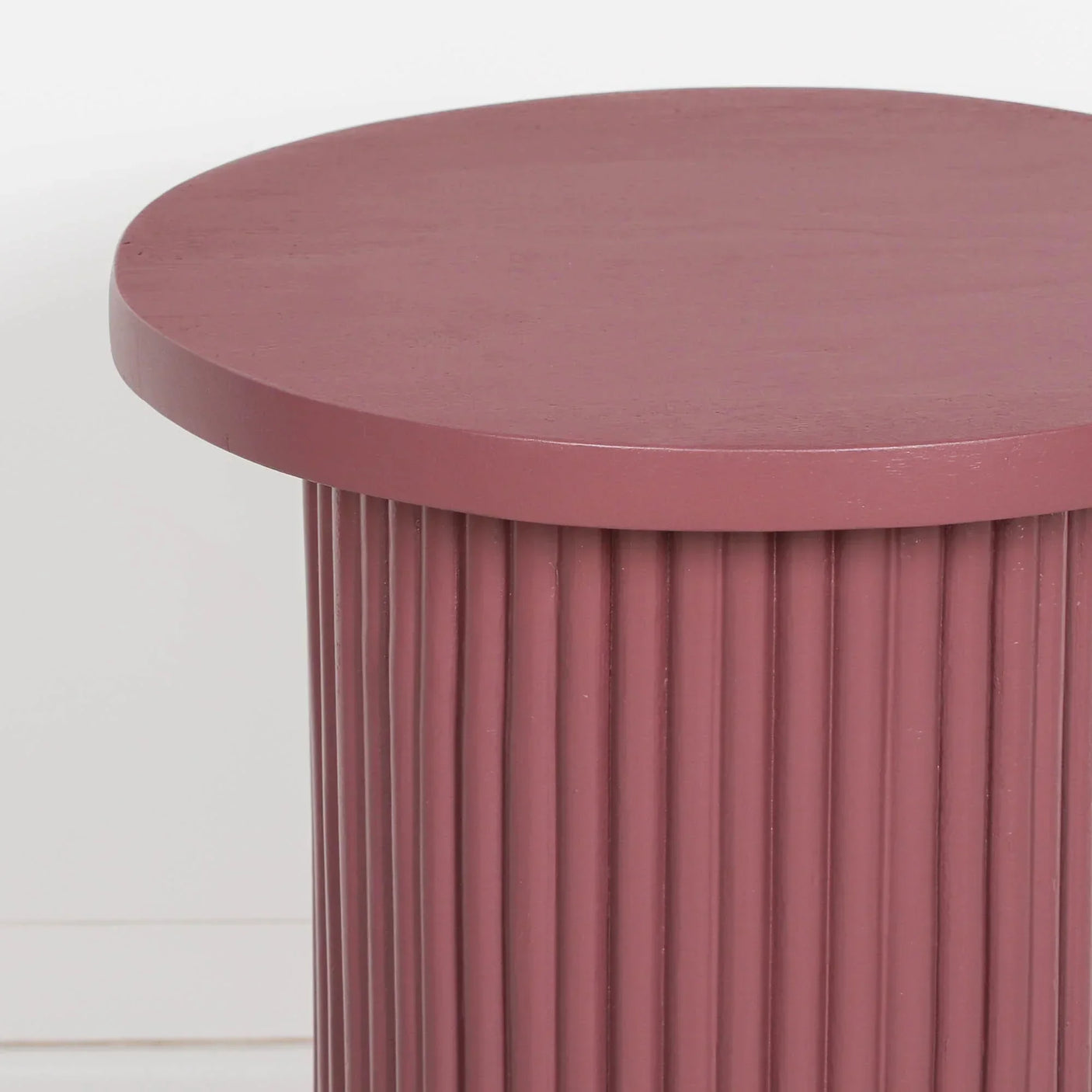 Plum side table with fluted cylindrical base and smooth round top, close-up view