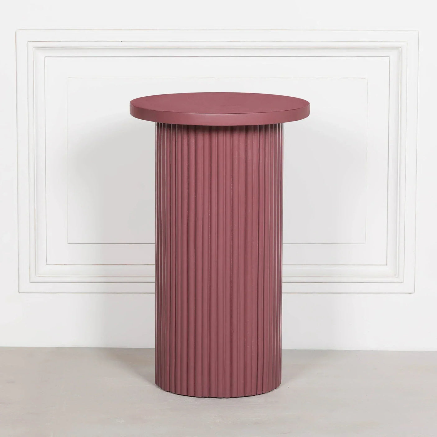 Round mauve side table with fluted base and smooth top against white wall