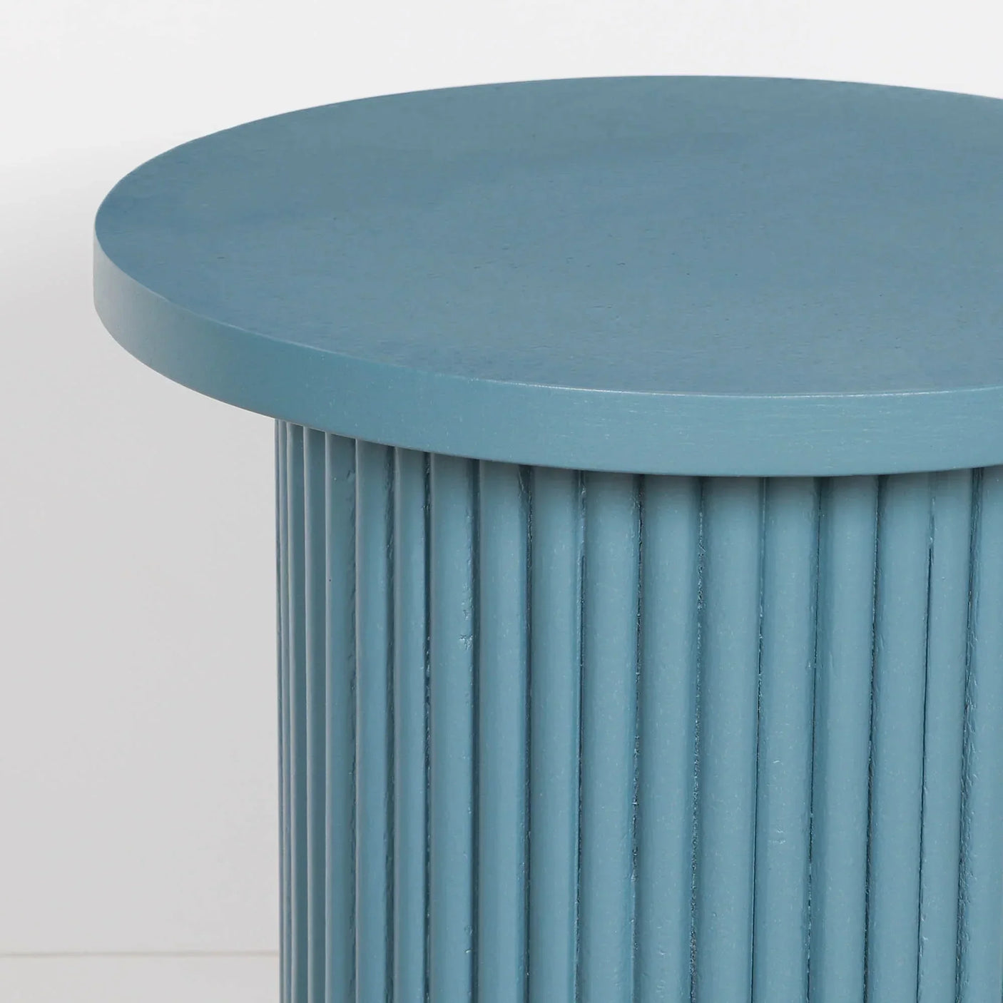 Blue round side table with fluted cylindrical base against white background