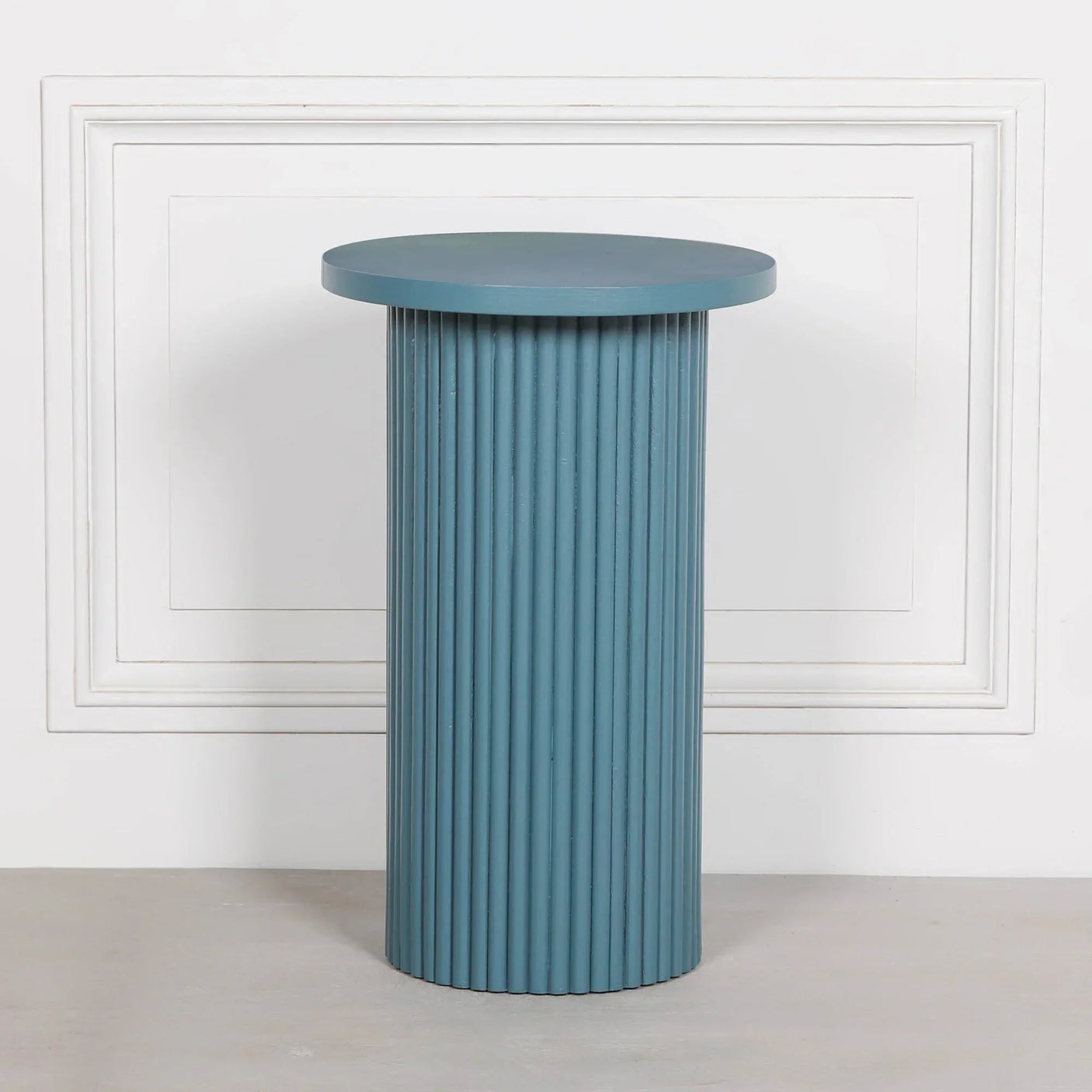 Blue fluted side table with round top against white wall paneling
