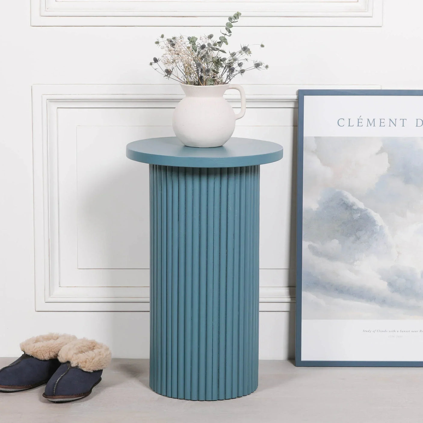 Blue ribbed side table with round top, white ceramic vase, dried flowers and framed wall art
