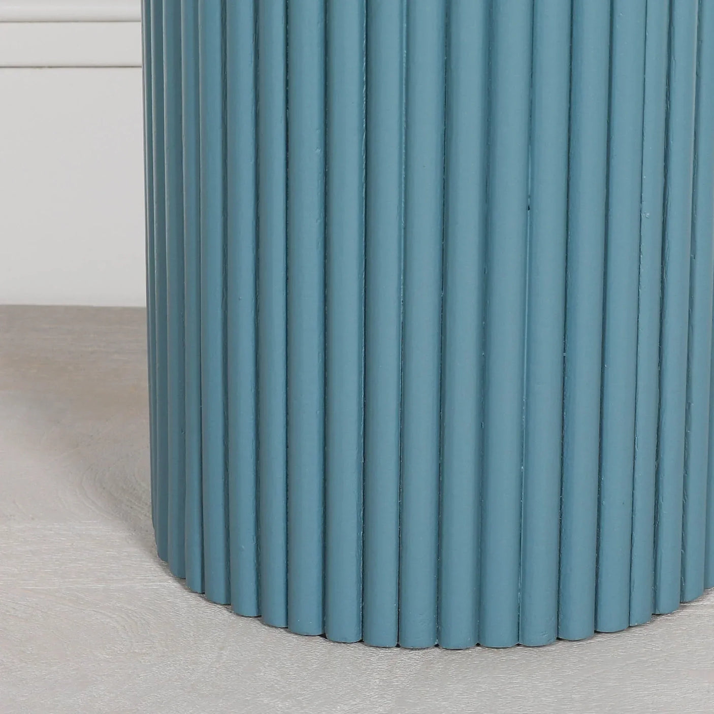 Blue ribbed side table base with vertical slats on light wood floor