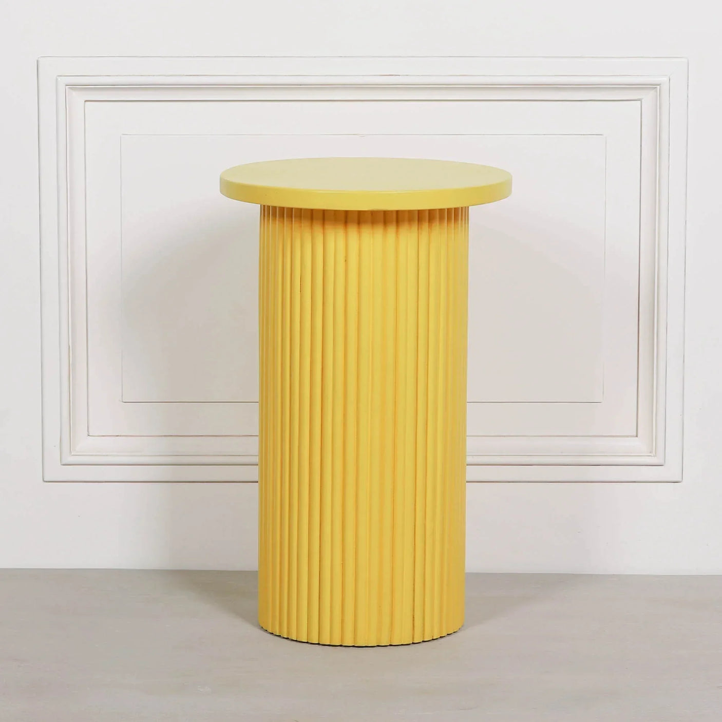 Yellow ribbed side table with round top and vertical groove detailing against white wall