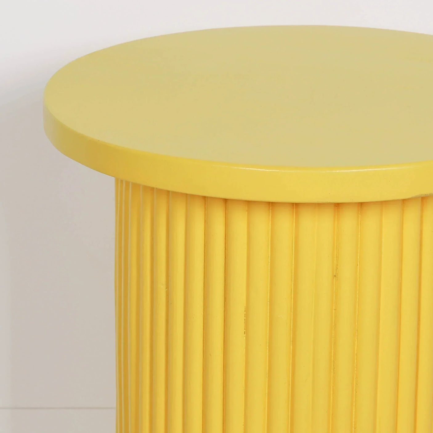 Yellow side table with round top and vertical ribbed base against white wall