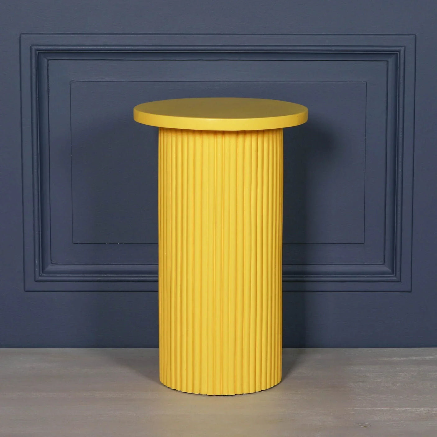 Yellow ribbed side table with round top against a dark blue paneled wall