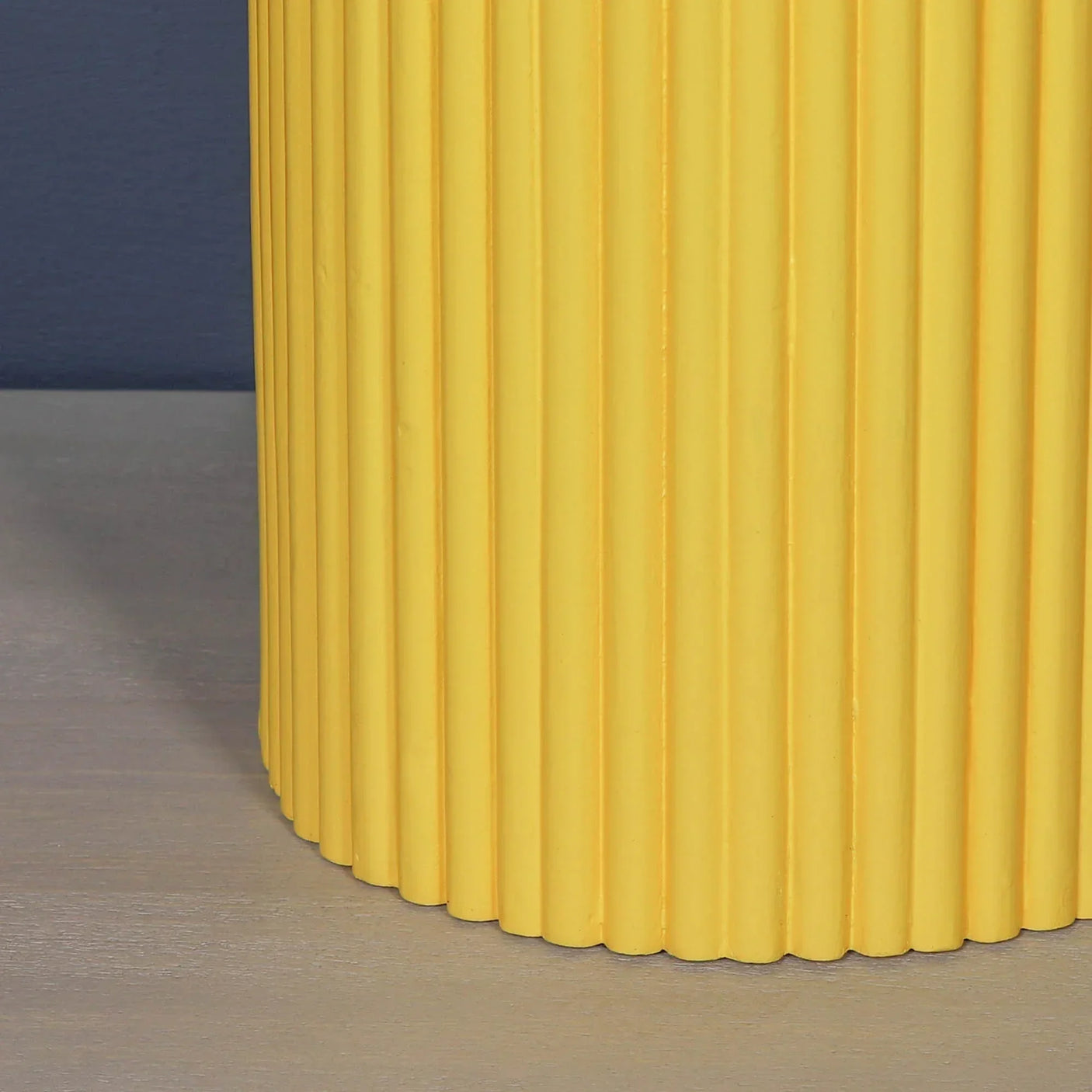 Yellow ribbed side table base against grey surface and blue wall