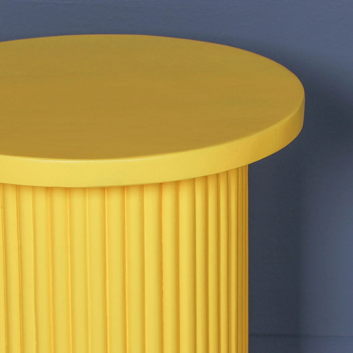 Yellow side table with fluted cylindrical base against blue wall