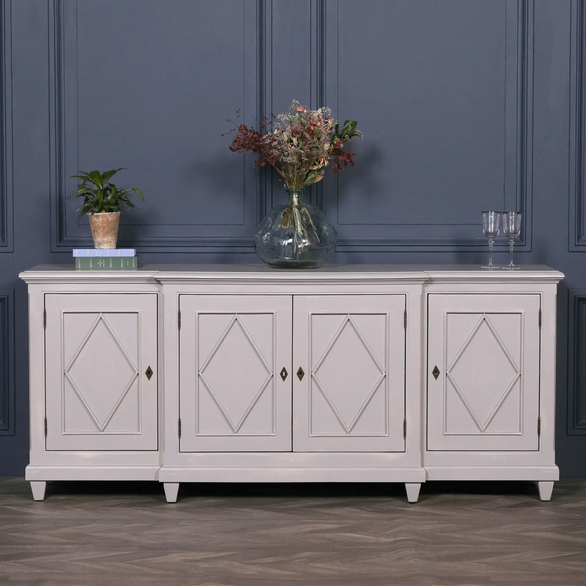 White wooden sideboard with diamond panel doors in living room, decorated with vase and plant