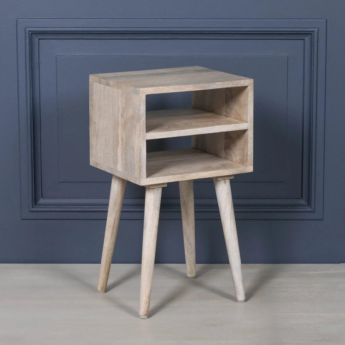 Light wood bedside table with open shelf and four angled legs against a blue wall