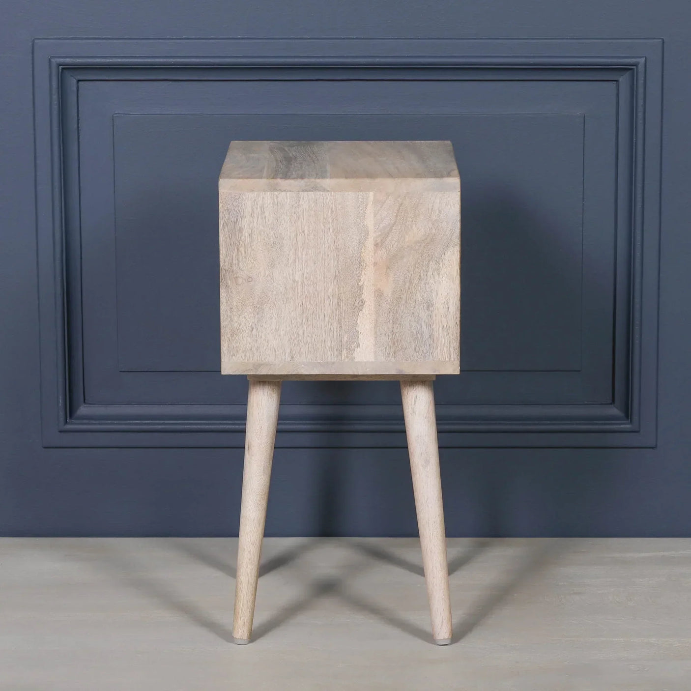 Natural wood bedside table with square body and angled legs against blue wall