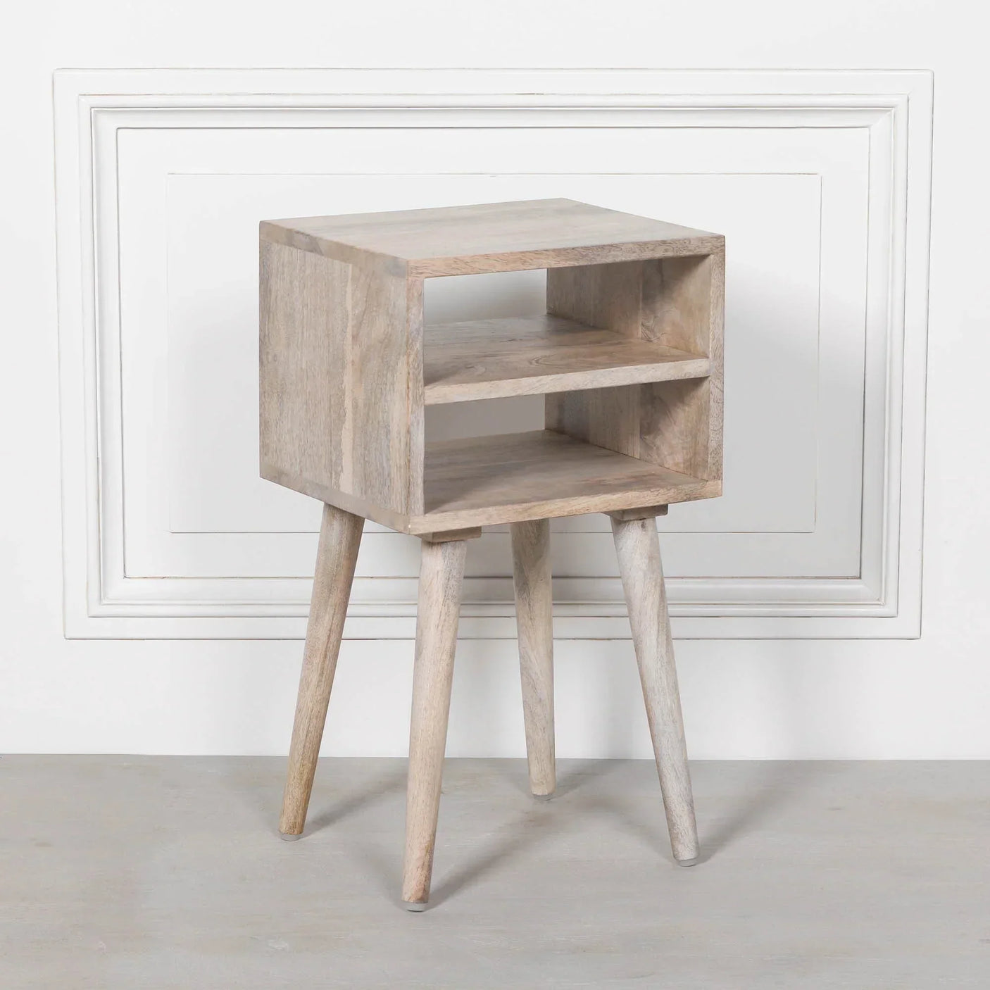 Light wood bedside table with open storage shelf and angled legs against white wall