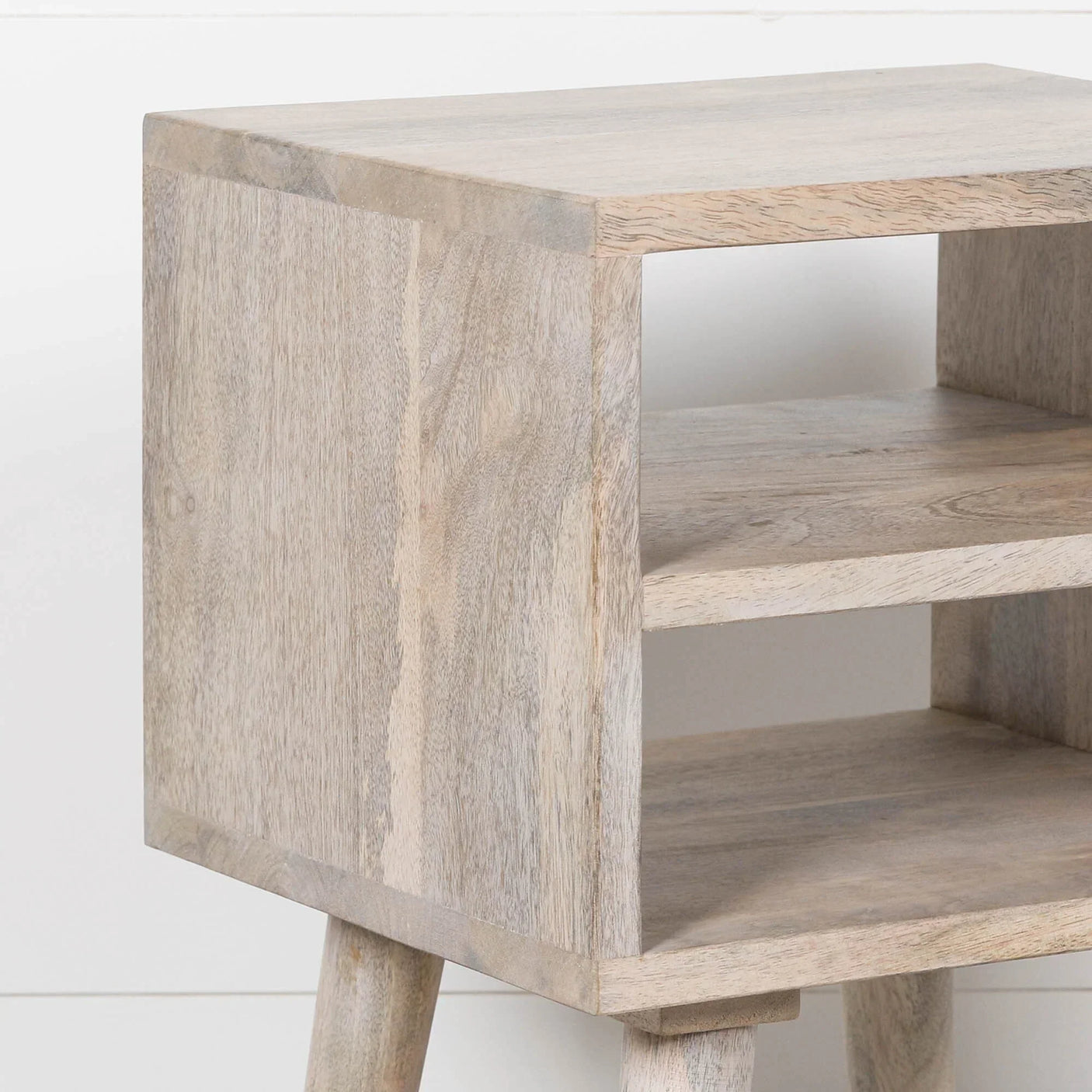 Light wood bedside table with open shelf and splayed legs, close side view