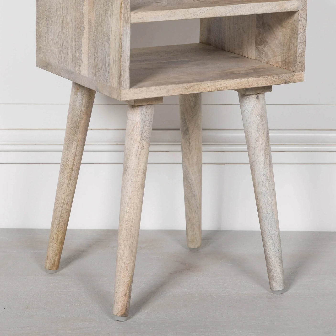 Light wood bedside table with angled legs and open shelf, close-up corner view