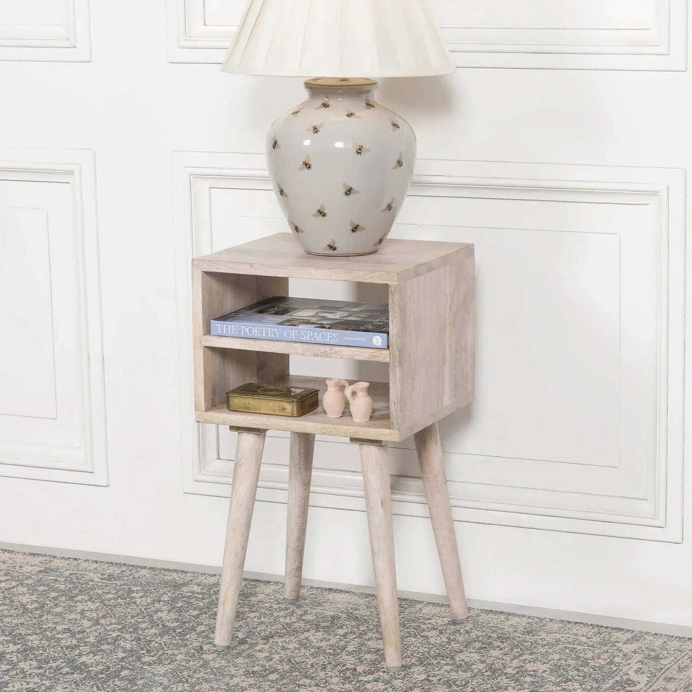 Light wood bedside table with open shelf, holding books and decor, styled with ceramic lamp
