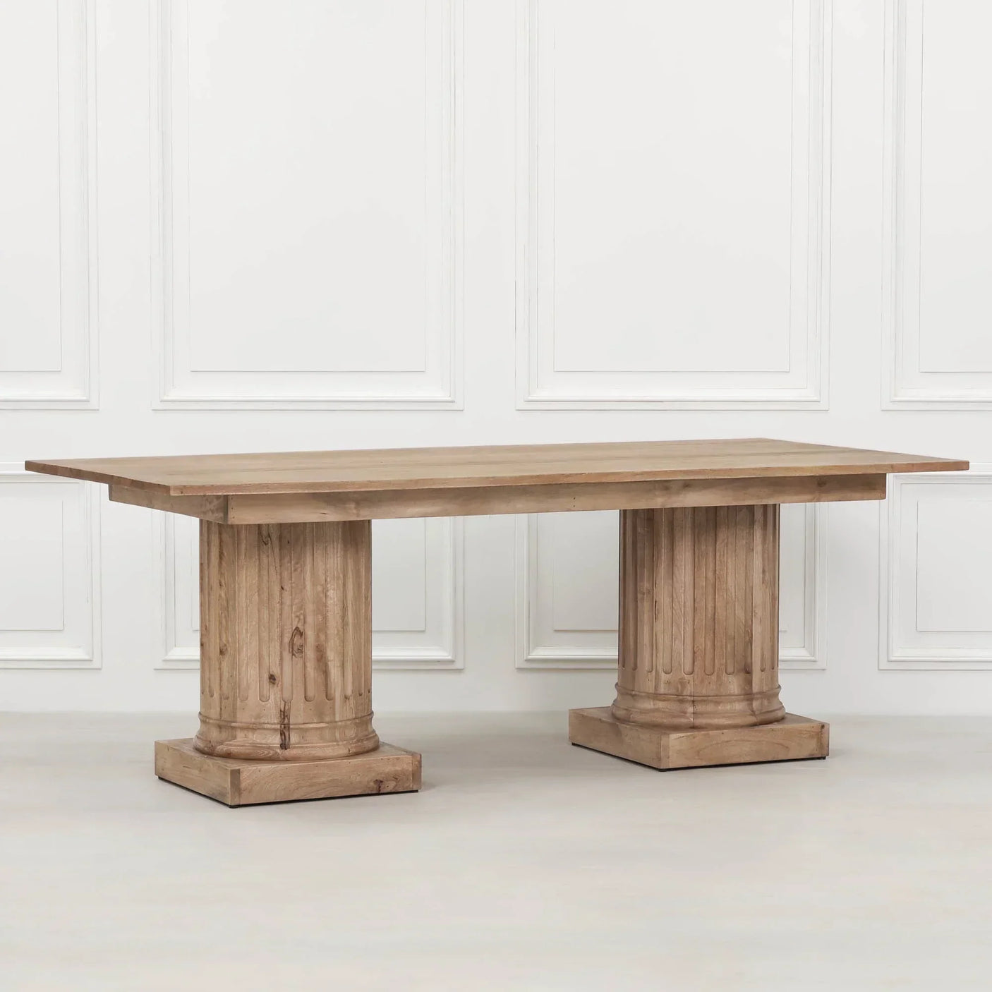 Rectangular wooden dining table with pillar style pedestal legs against white panel wall