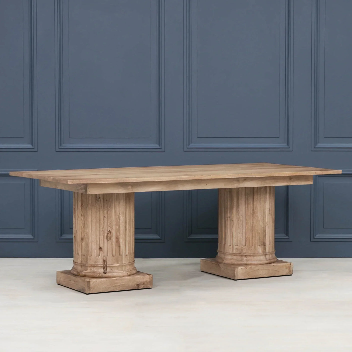 Solid wood dining table with twin pillar bases against blue panel wall