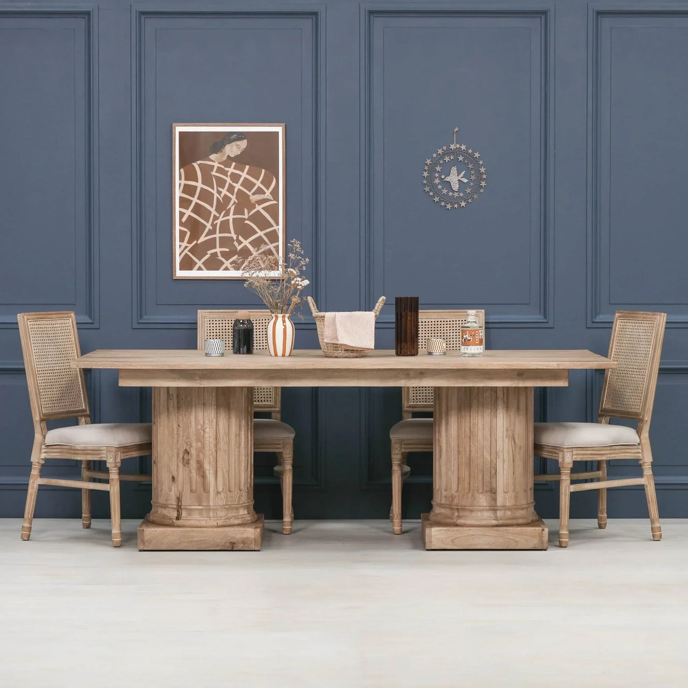 Rectangular wooden dining table with pillar legs and rattan-back chairs in blue-walled room