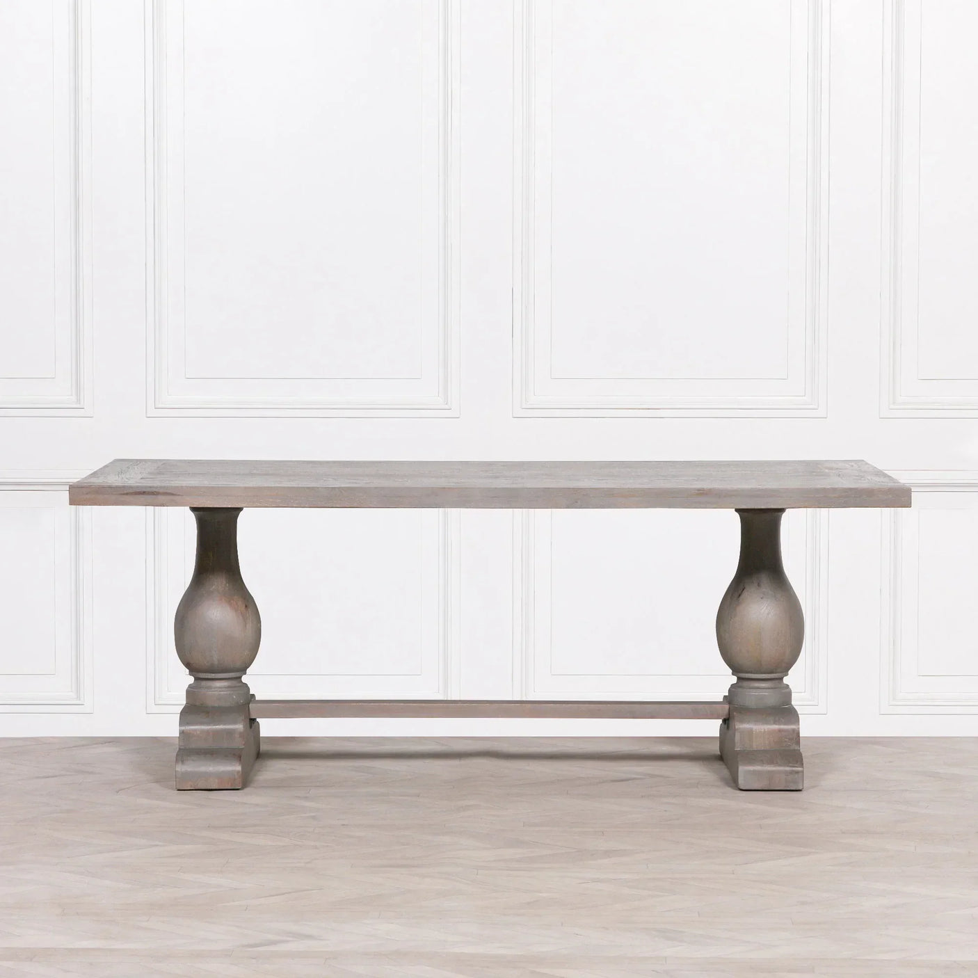 Rectangular wooden dining table with turned pedestal legs and light finish against panelled wall