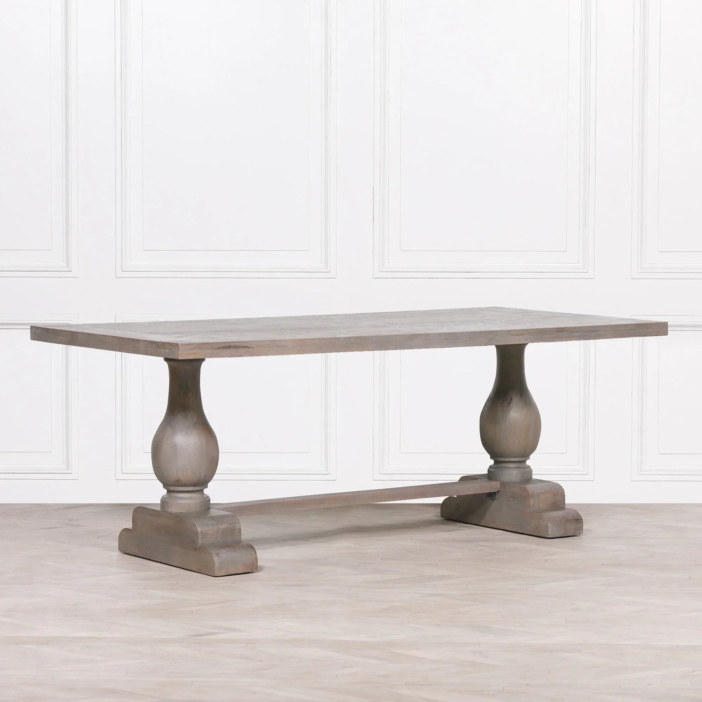 Rustic wood dining table with trestle base and carved pedestal legs on light floor