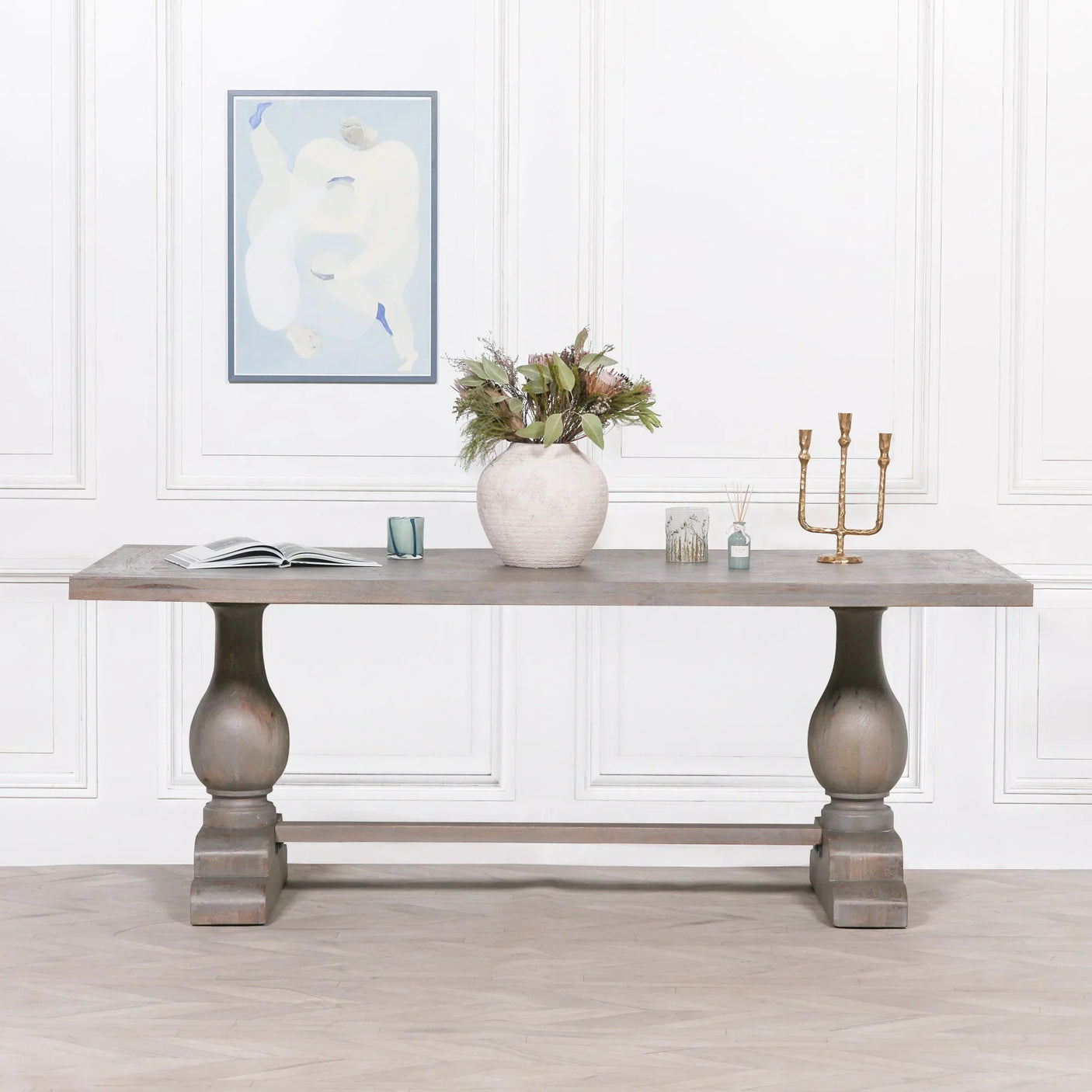 Rustic wooden dining table with pedestal legs, vase, candleholder and decor accents