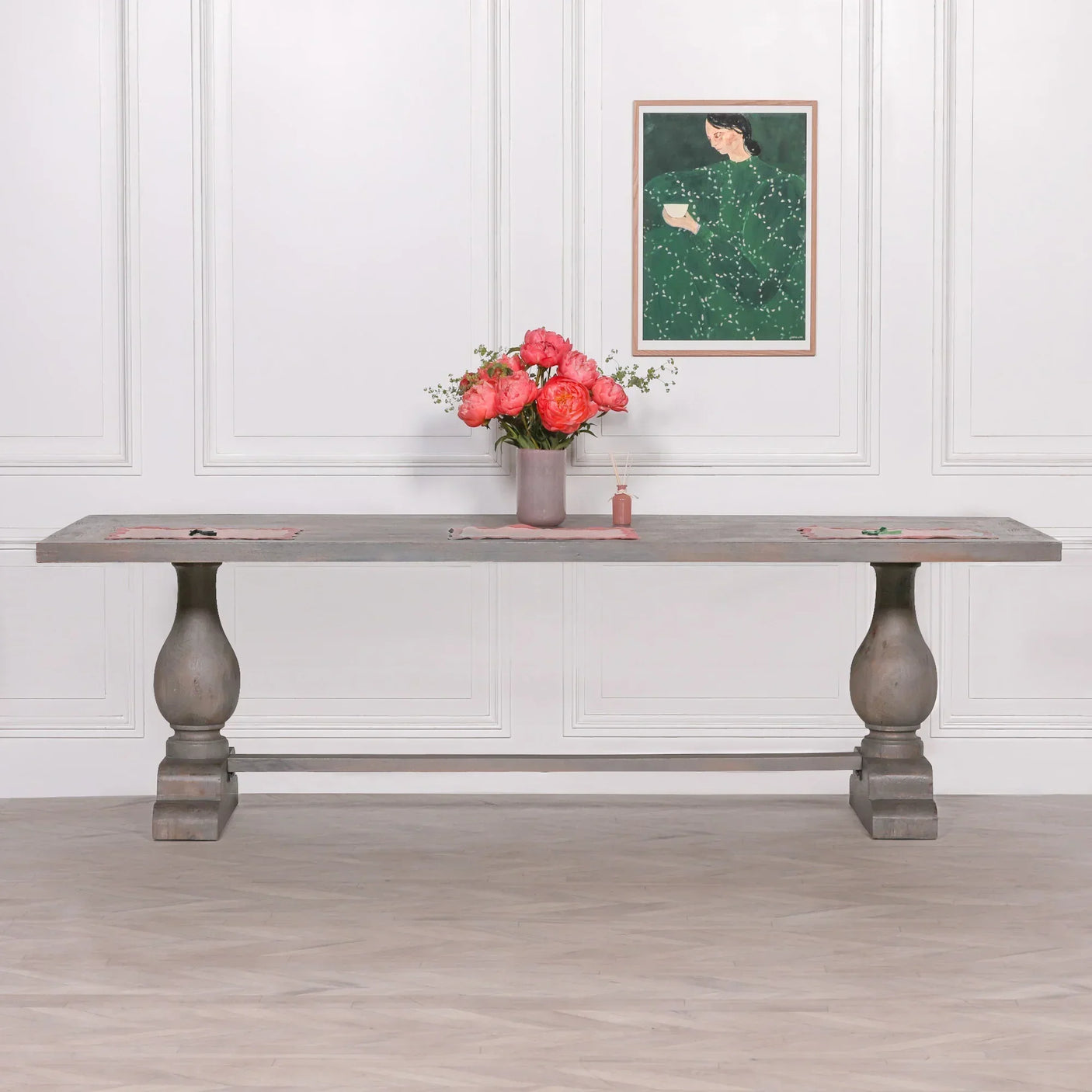 Rustic wooden dining table with wide top, pedestal legs, and pink flowers in vase