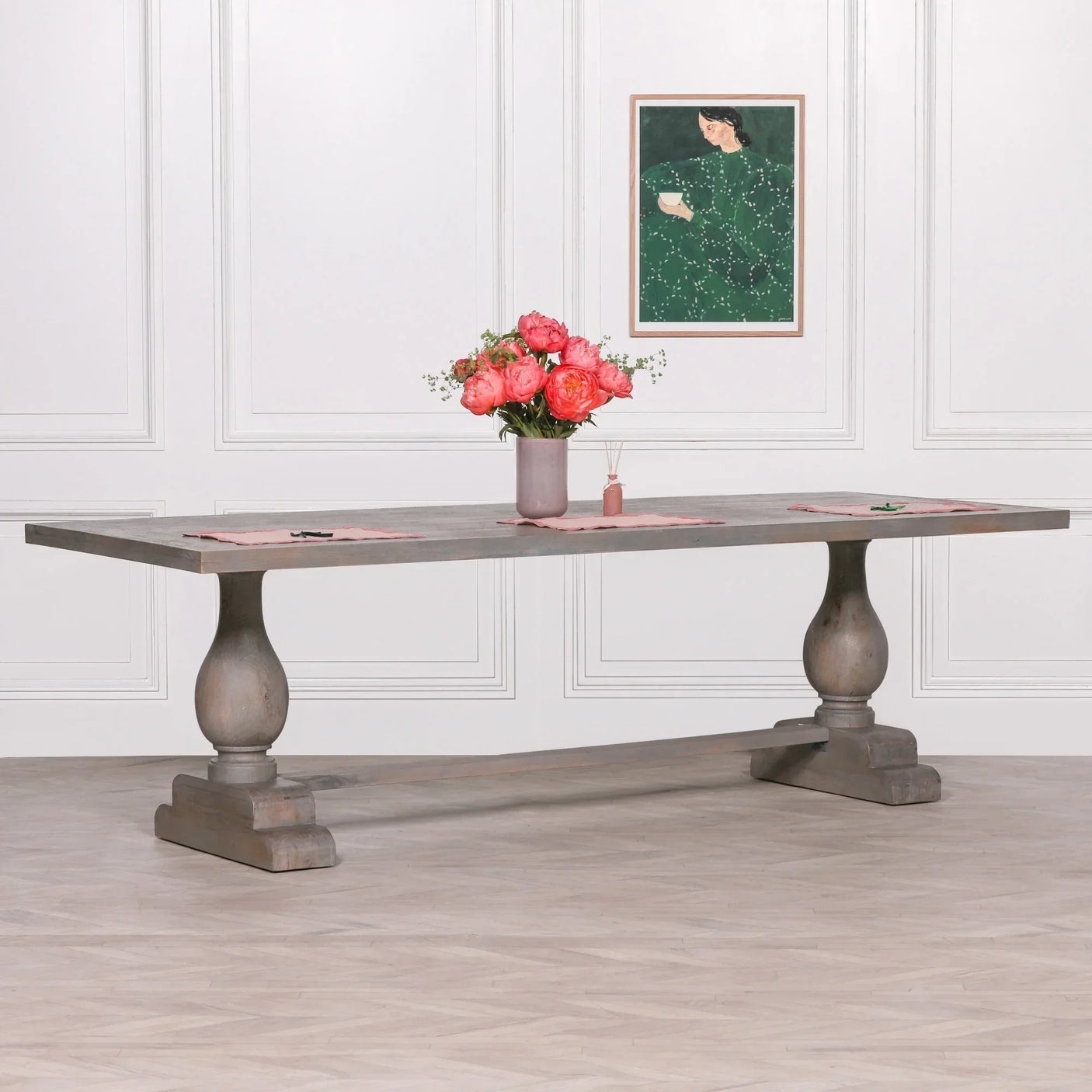 Wooden dining table with pedestal legs and vase of pink flowers in bright room