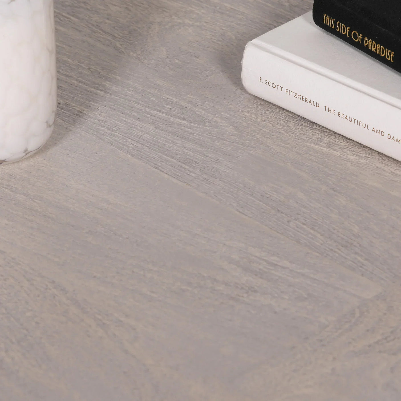 Grey wood coffee table surface with books and a white glass candle holder