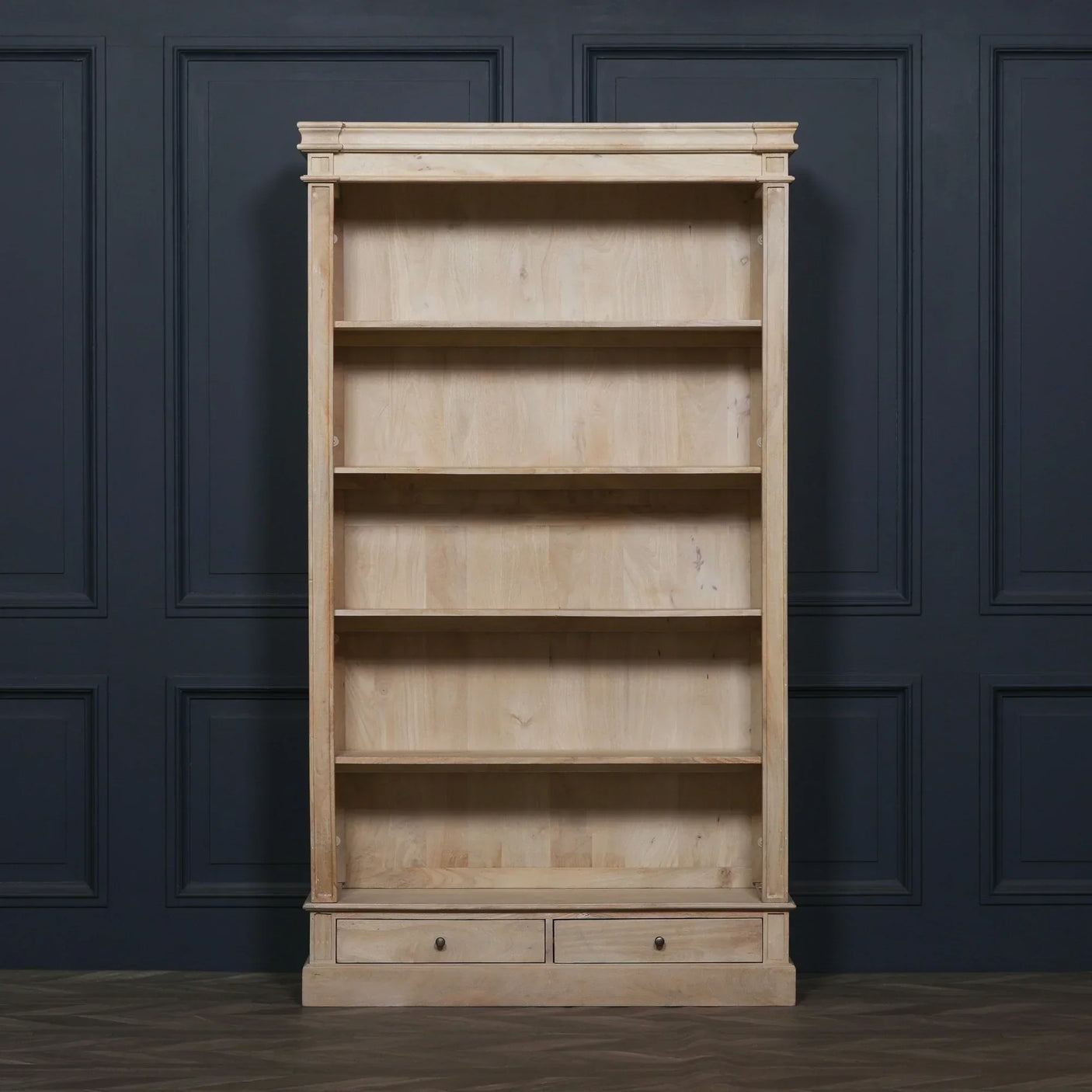 Natural wood bookcase with four open shelves and two drawers against dark panelled wall