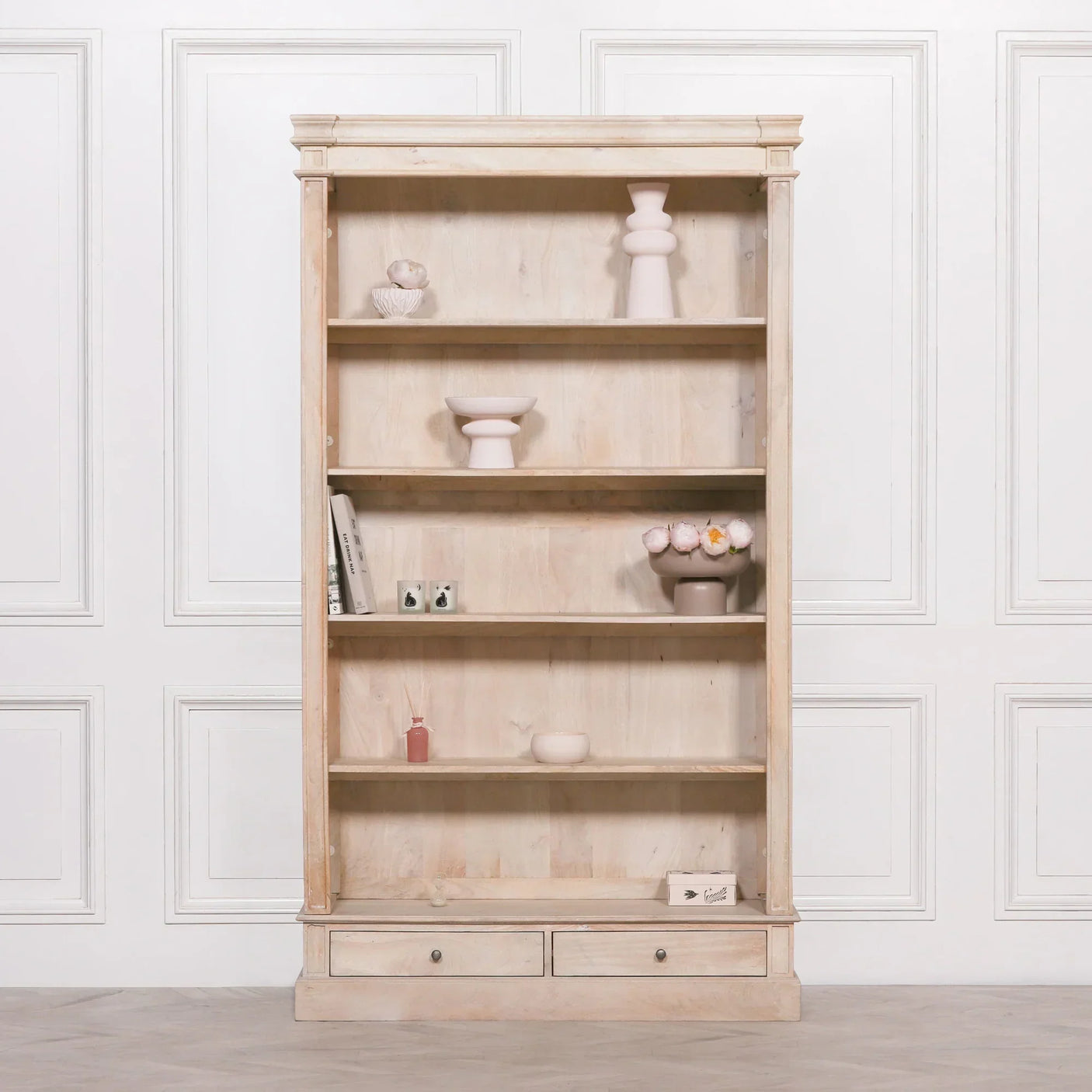 Light wood bookcase with open shelves, two drawers, and decorative vases and books