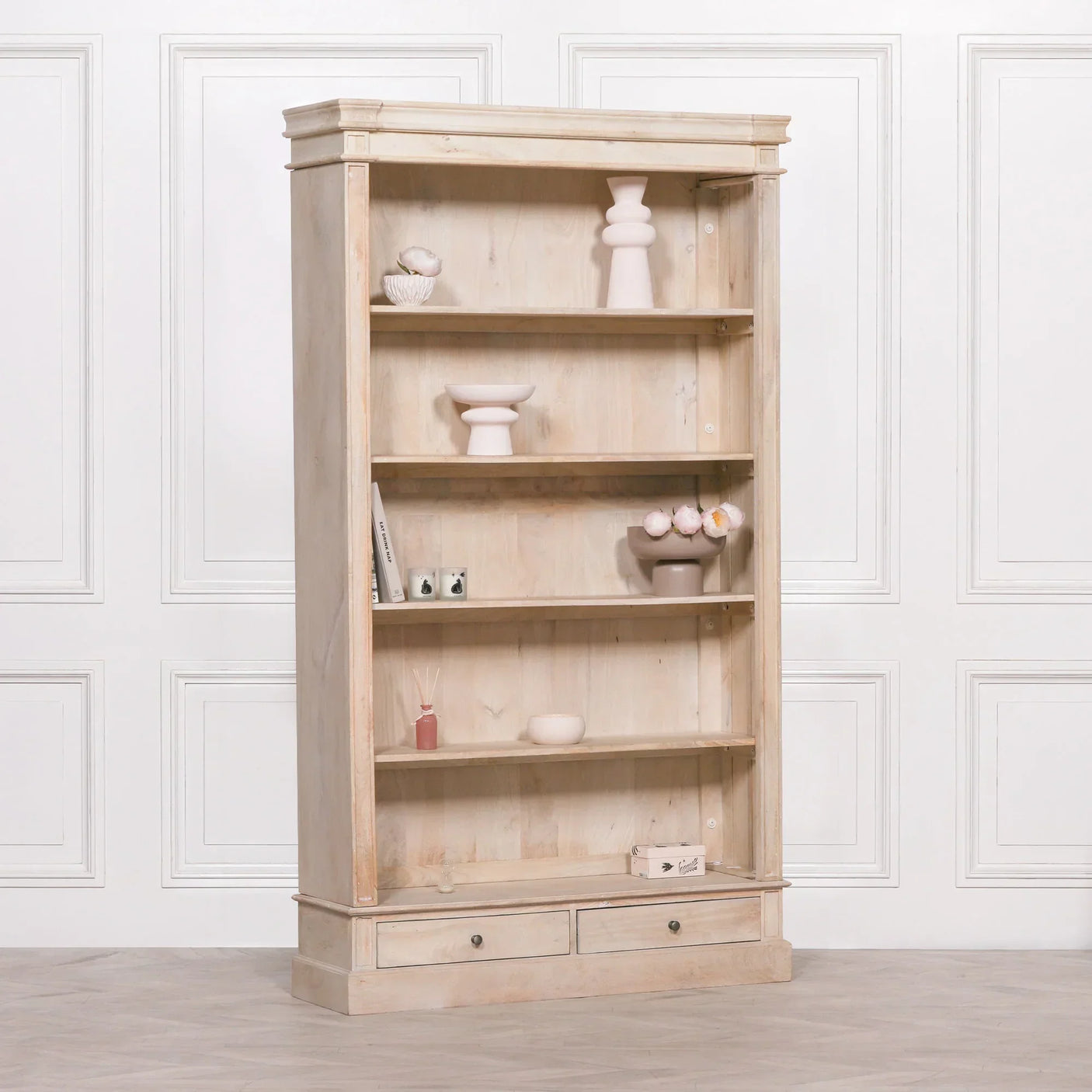 Light wood bookcase with four shelves, two drawers, and decorative items in a classic room