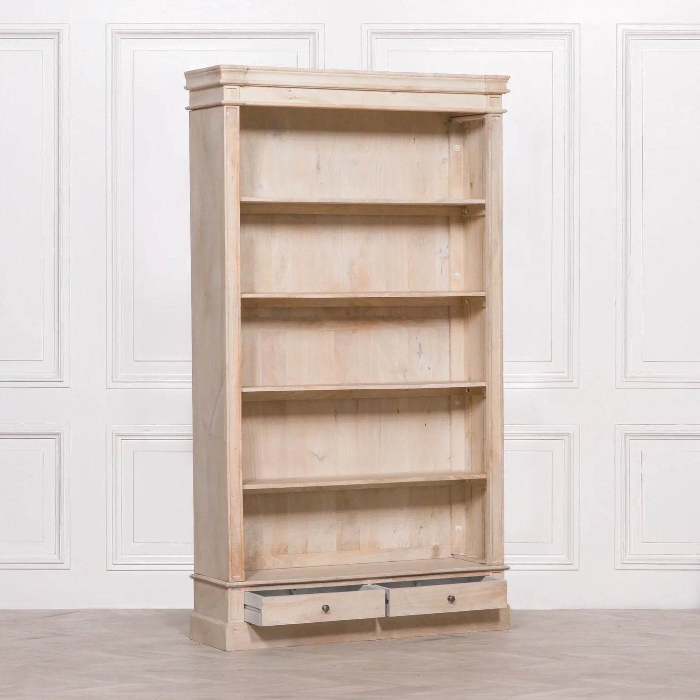 Light wood bookcase with four shelves and two lower drawers against a white panel wall