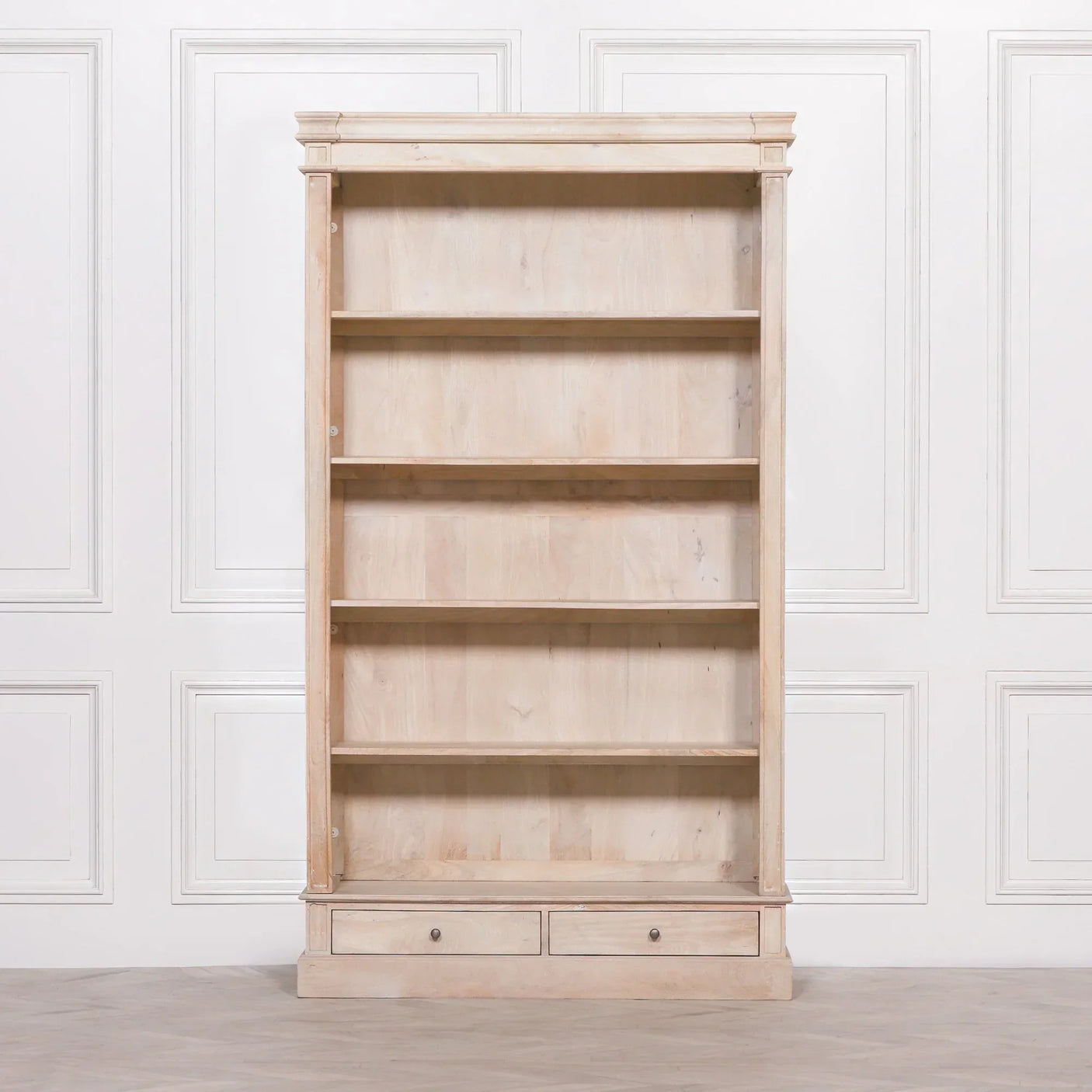 Light wood bookcase with four shelves and two drawers, set against a white panel wall