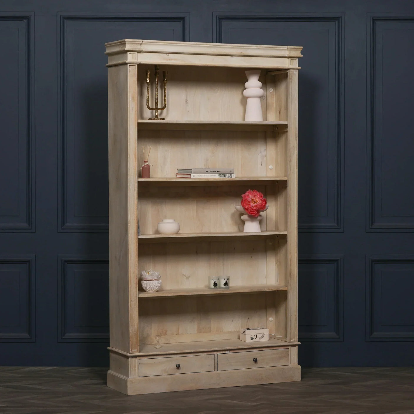 Light wood bookcase with shelves, two drawers, decorative items and books against dark wall