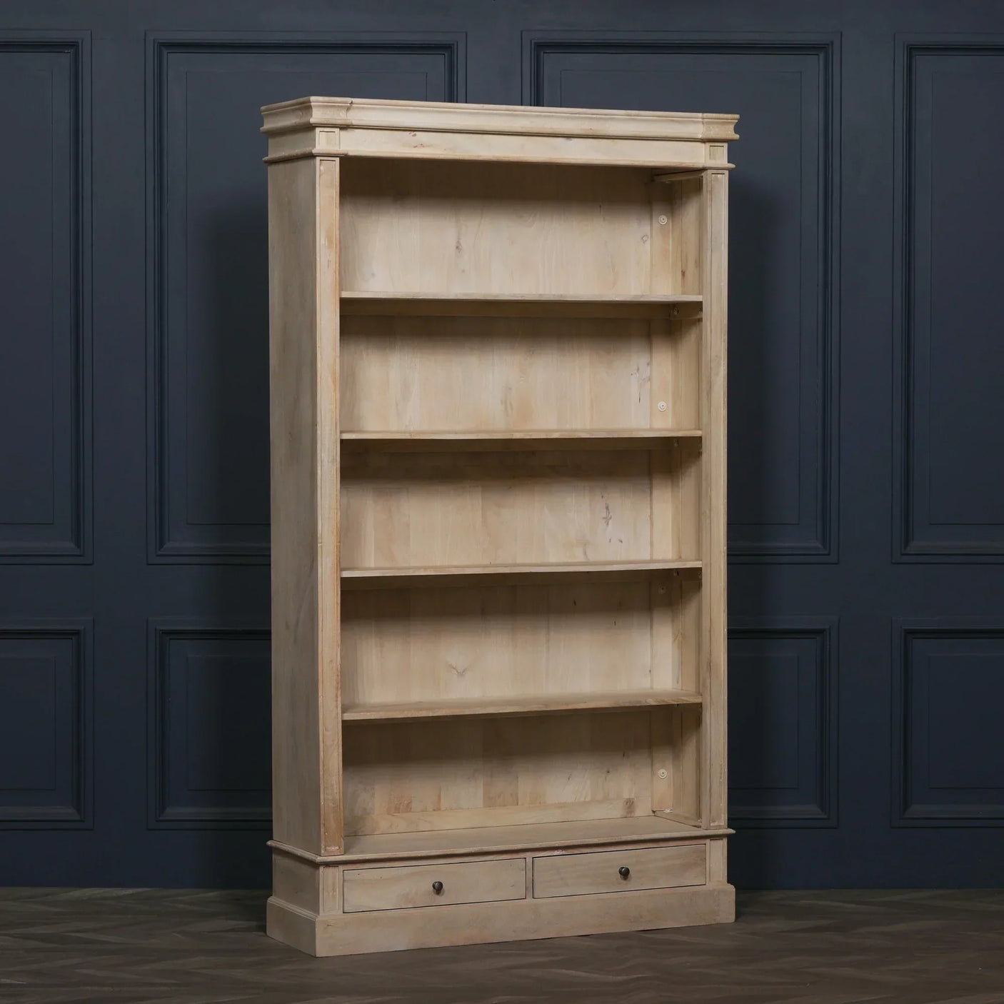 Natural wood bookcase with four shelves and two drawers against dark panelled wall