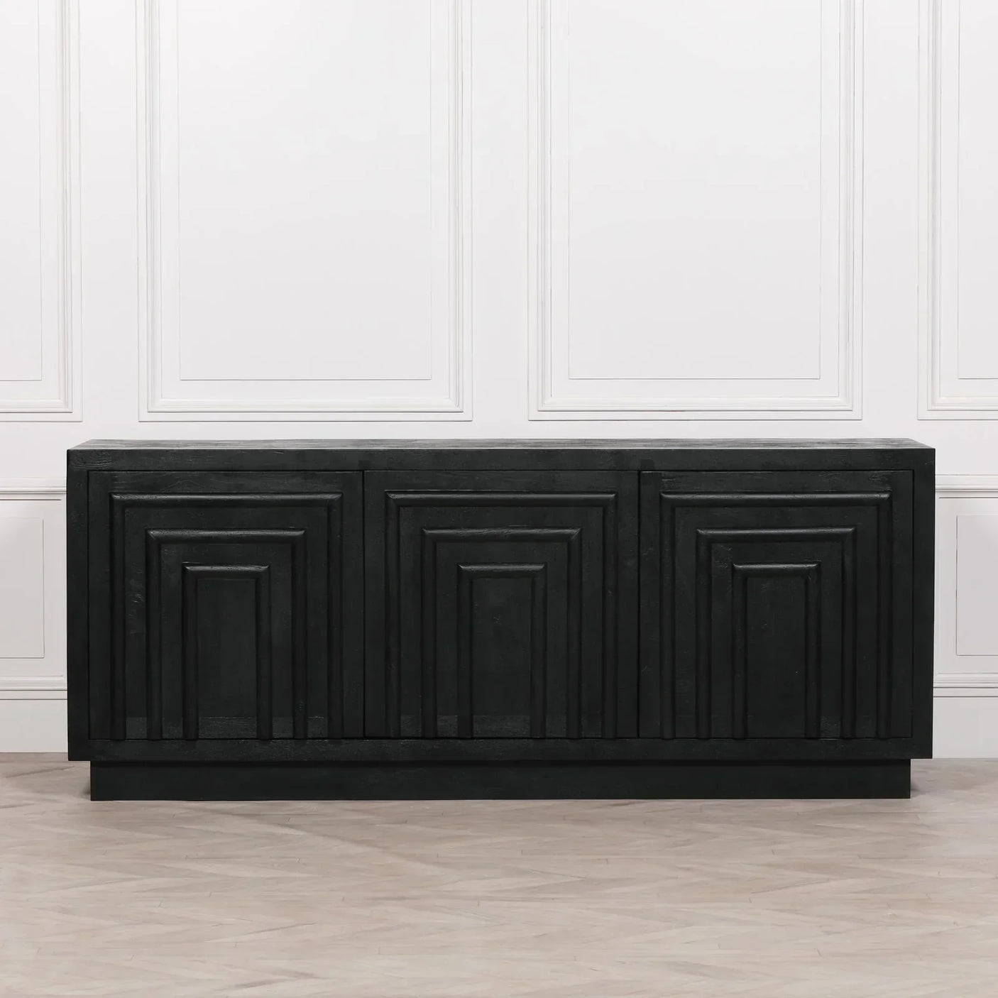 Black wooden sideboard with geometric panel doors against white wall and light wood floor
