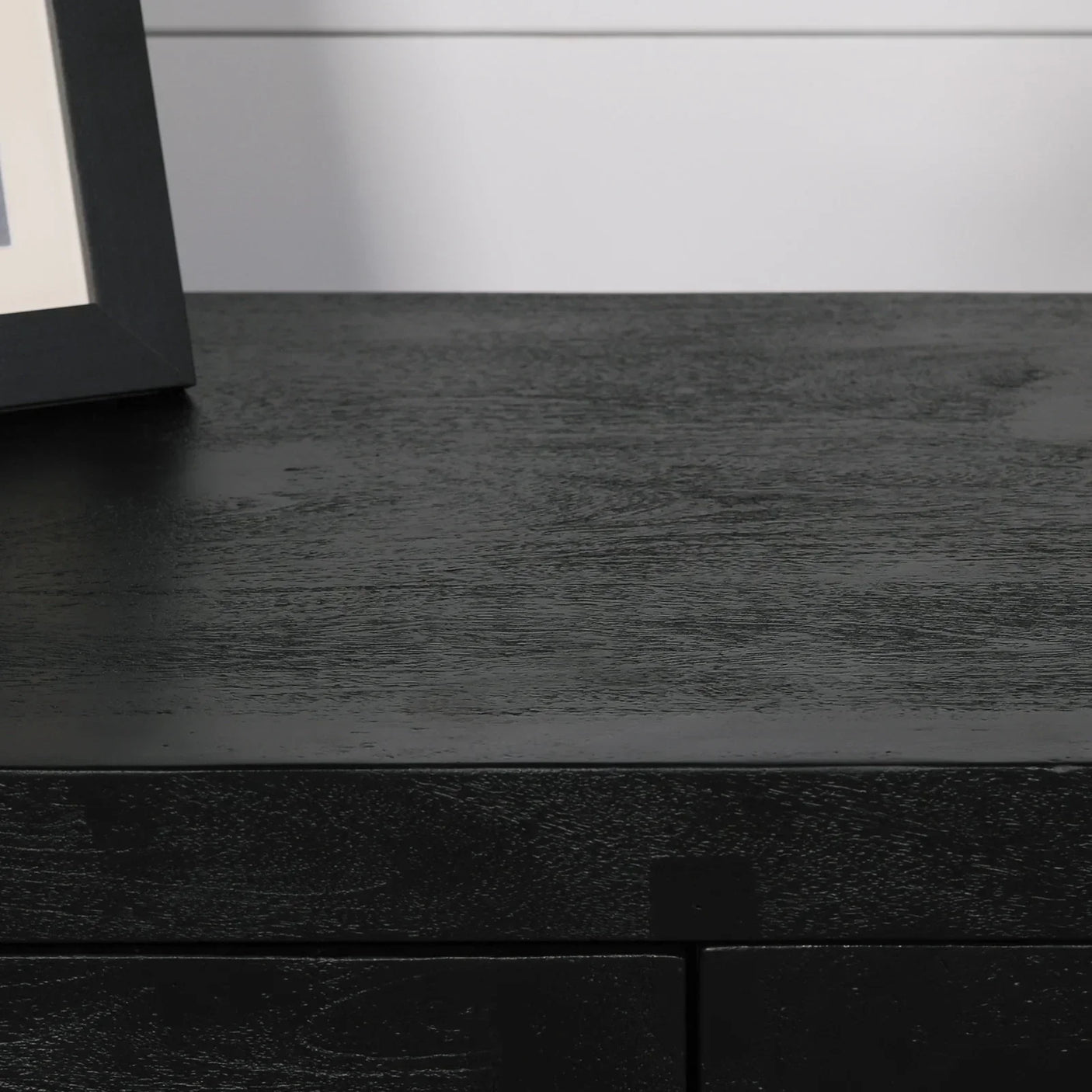 Black wood sideboard top surface with visible wood grain and corner of photo frame