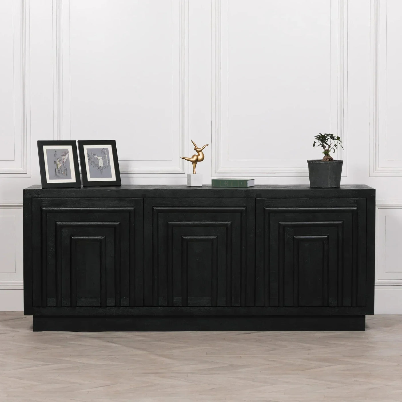 Black sideboard with geometric panel doors, decor items and plant on top against white wall
