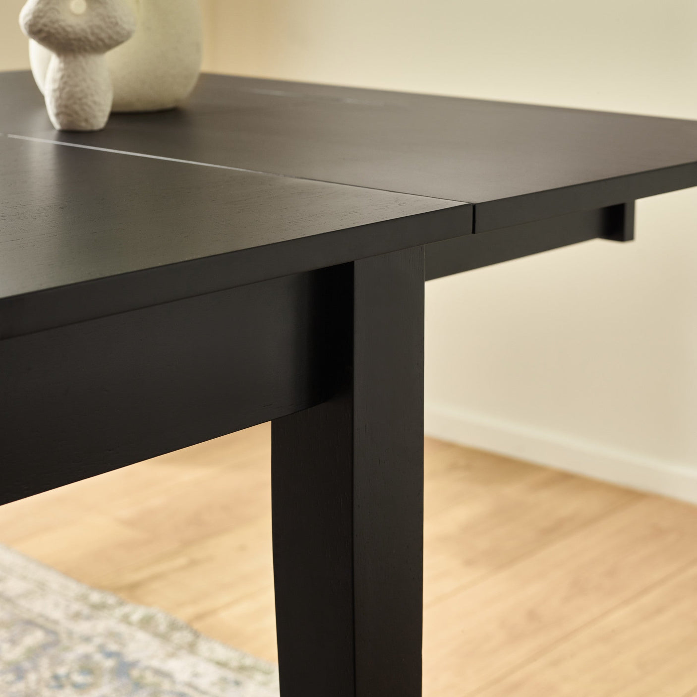 Black rectangular dining table fully extended, focusing on neat seam and wood grain on tabletop