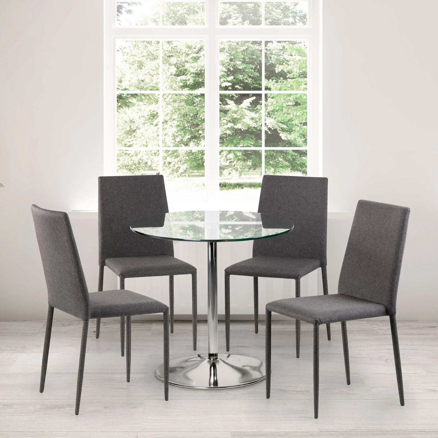 Round glass dining table with chrome base and four grey fabric dining chairs in bright room