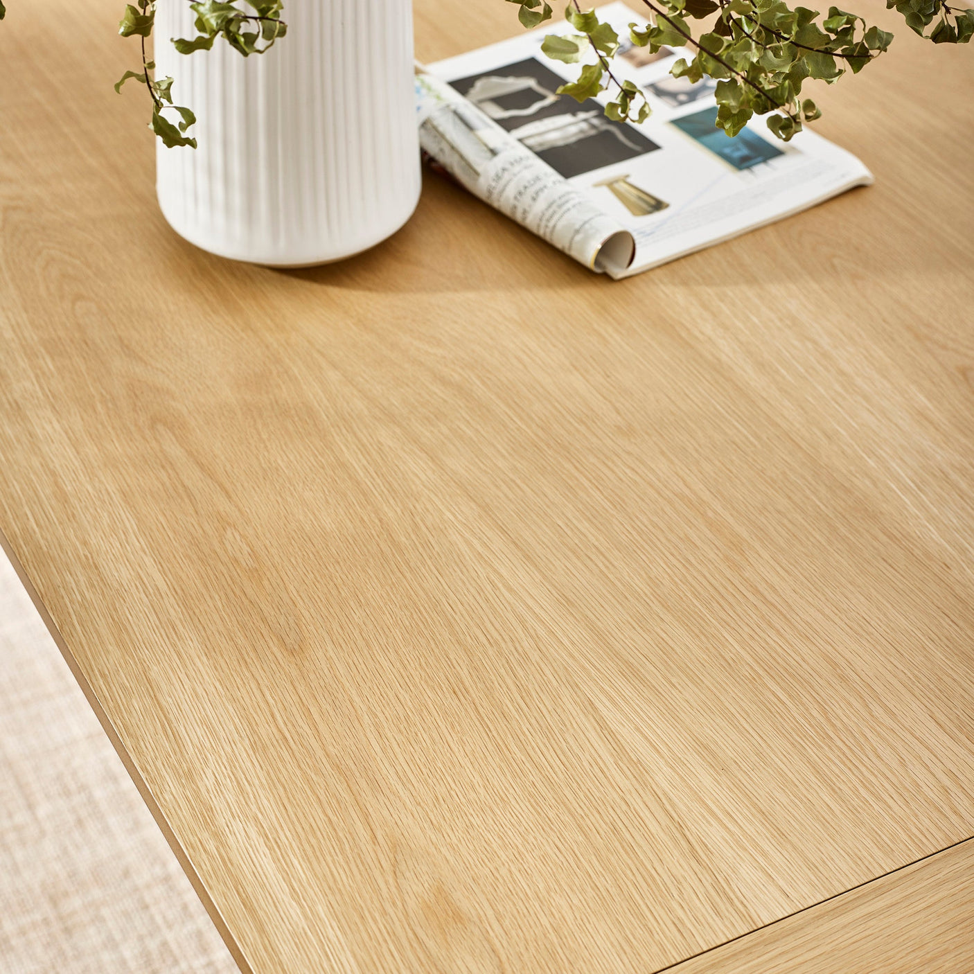 Close-up of smooth light wood grain tabletop with a white vase and rolled magazine on it