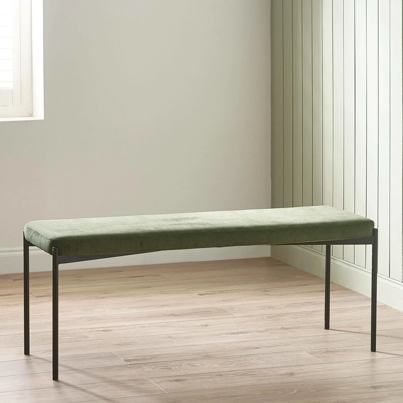 Green velvet bench with slim black metal legs on light wood floor in modern room